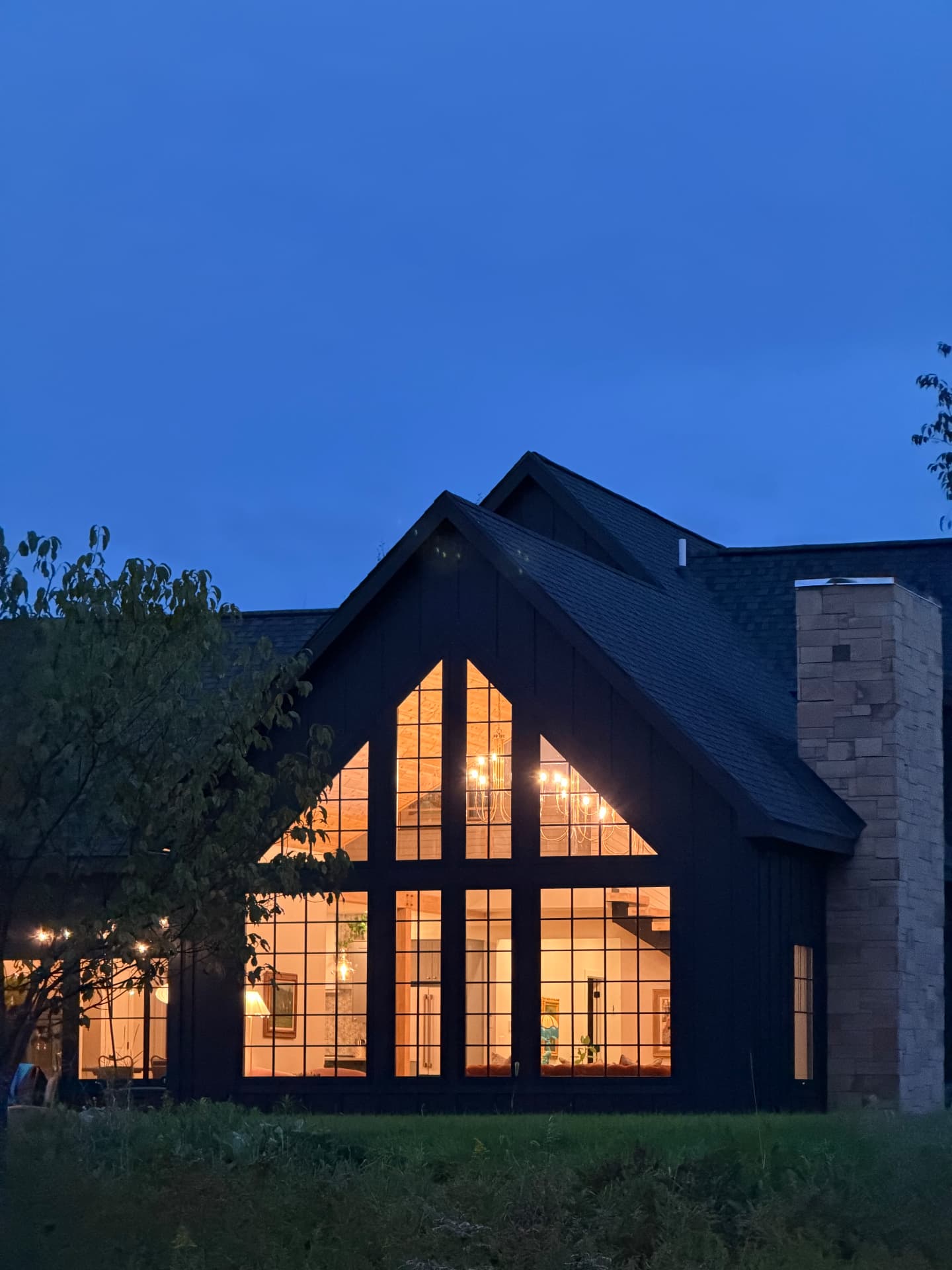 The gabled house lit from within under a deep blue evening sky