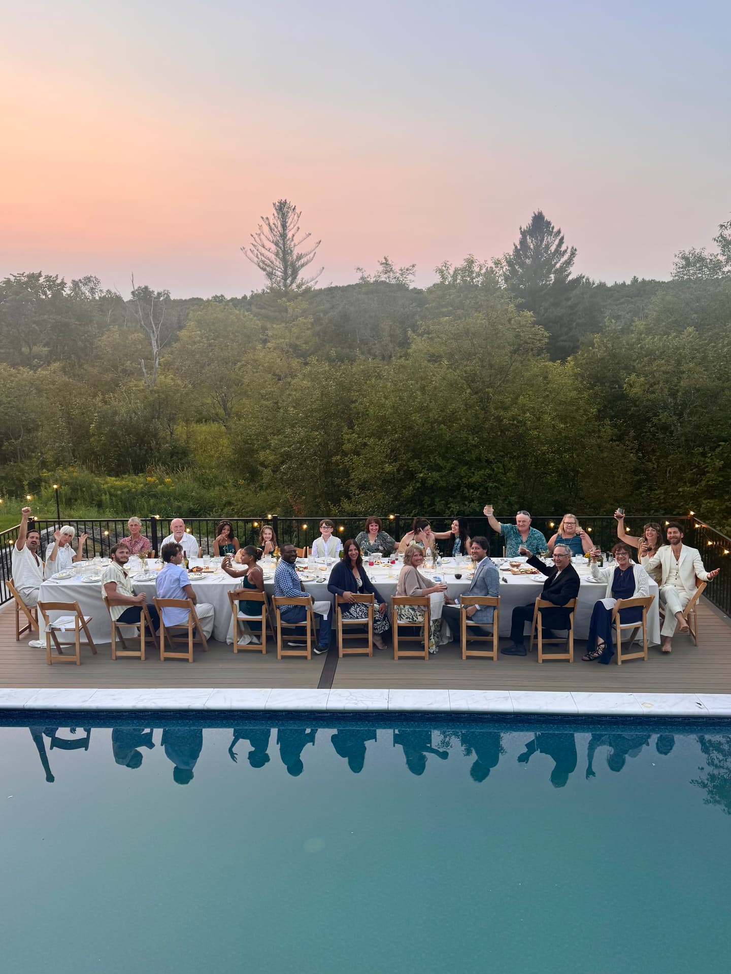 A long table of guests at dinner beside the pool at sunset