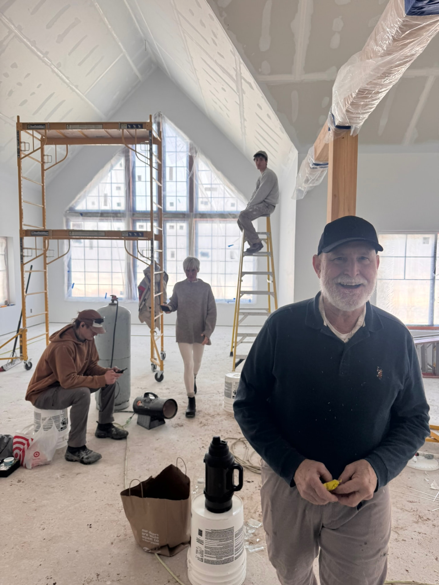 Big D smiling in the unfinished great room while the family works behind him