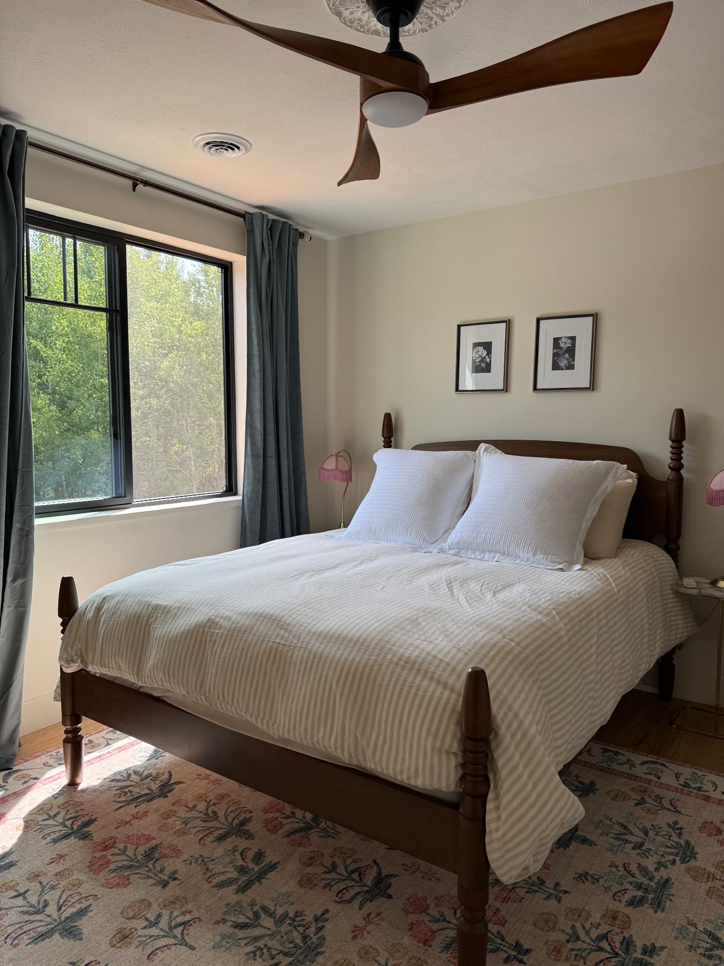 A bedroom with a wood-framed bed and striped linens by the window