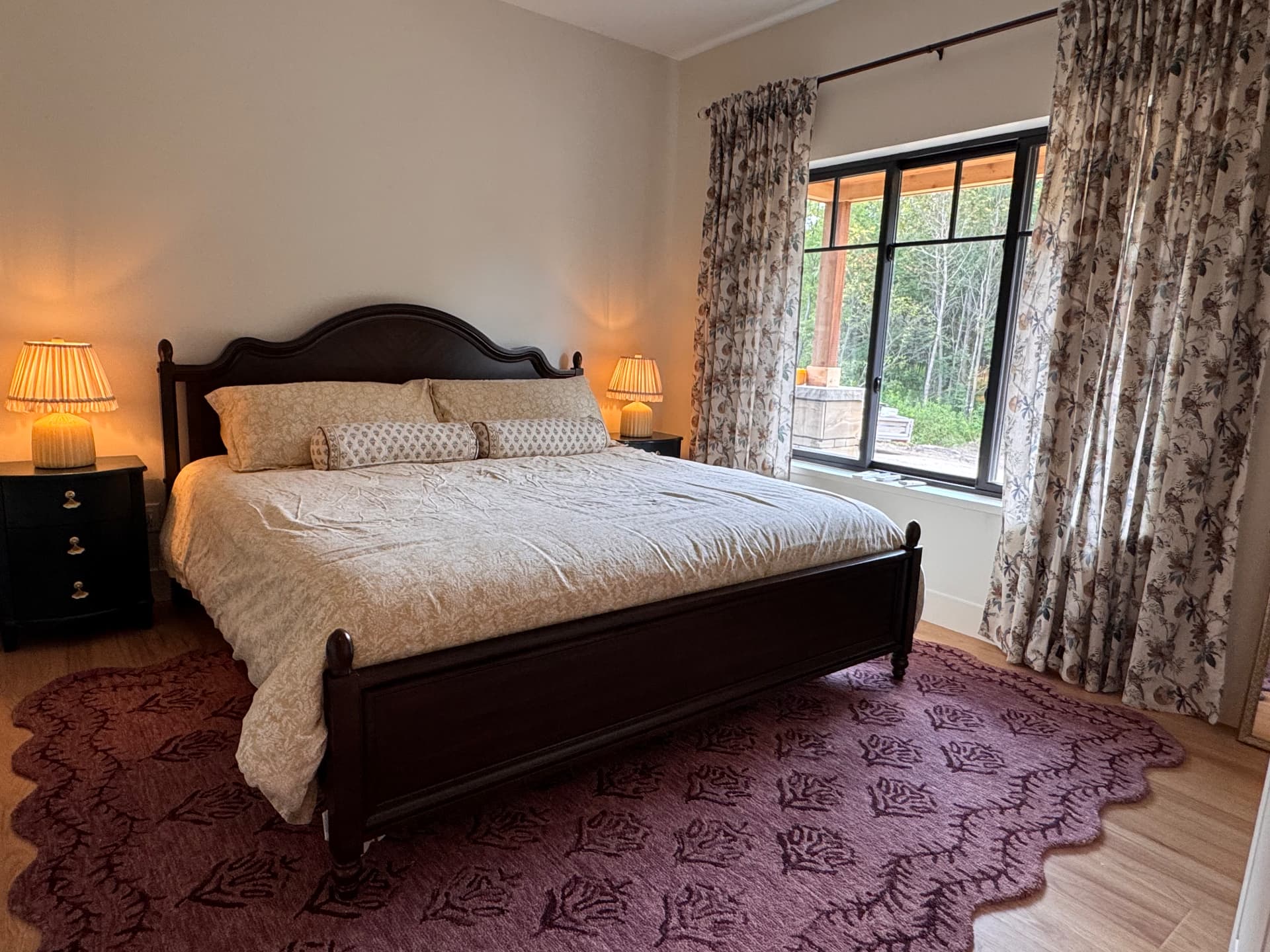 A dark-wood bed lit warmly with a view of the woods