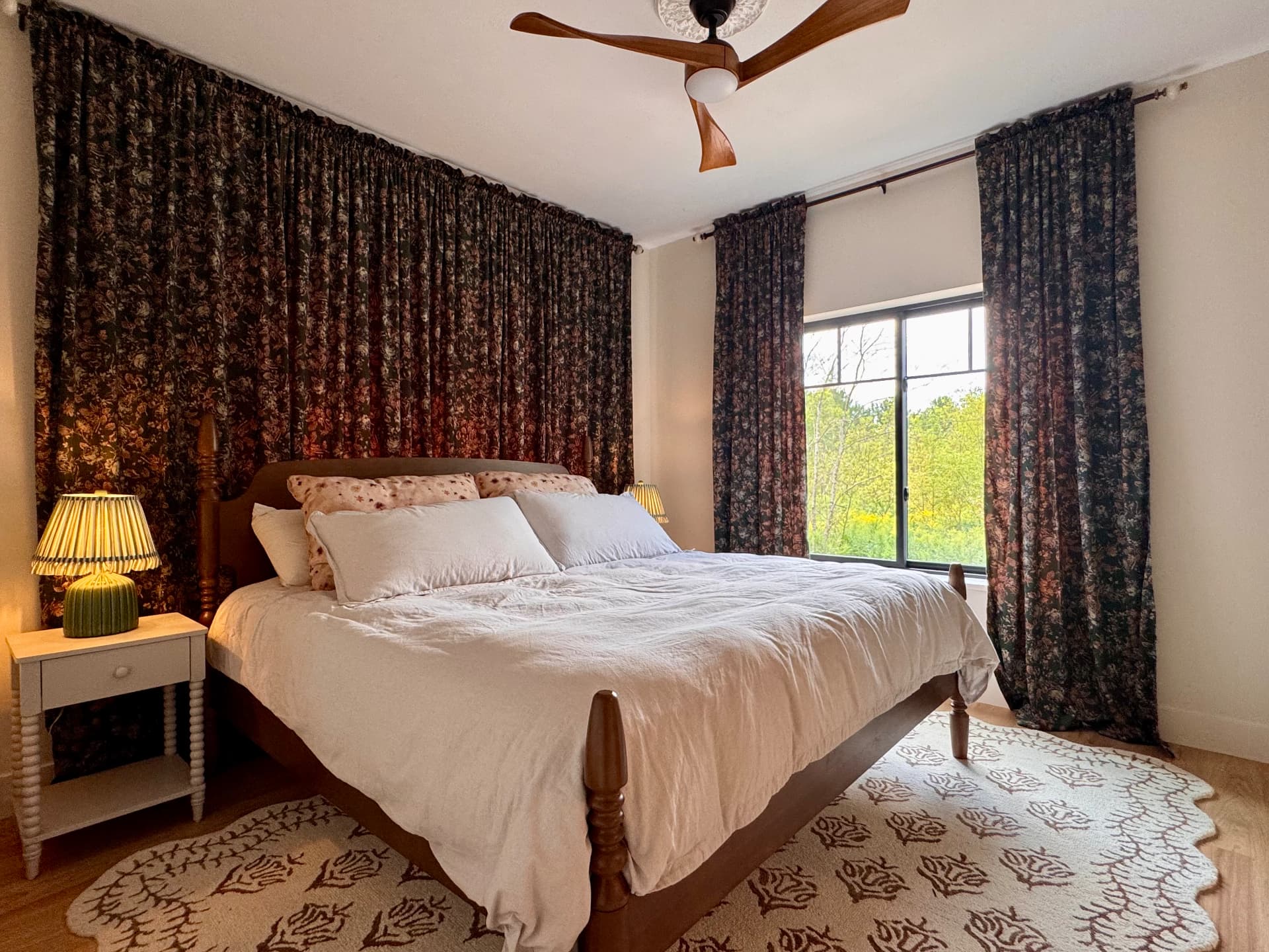A wooden bed with patterned curtains looking out over the field