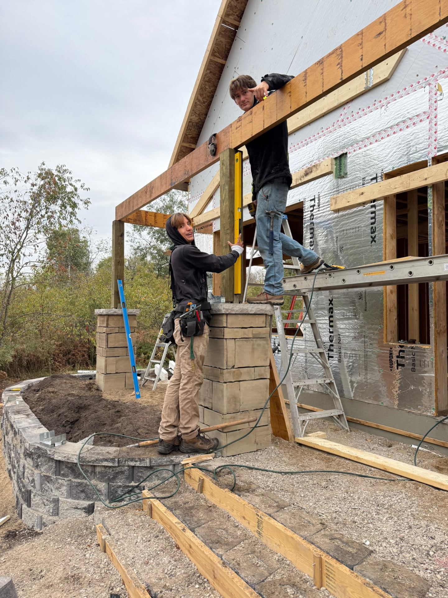 Two builders smiling while setting a post level against the framed gable