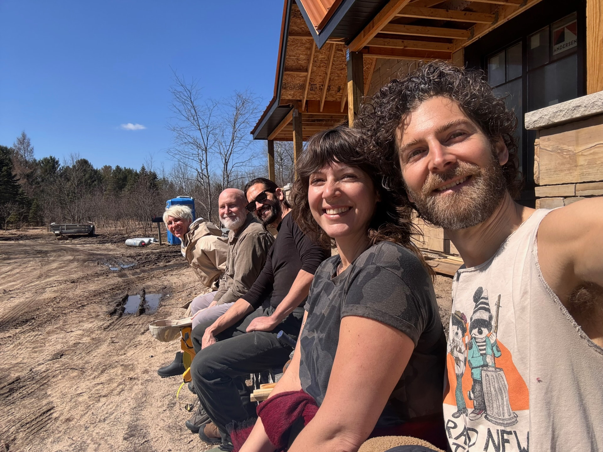 Five of the crew sitting along the retaining wall of the build site in the sun, everyone grinning