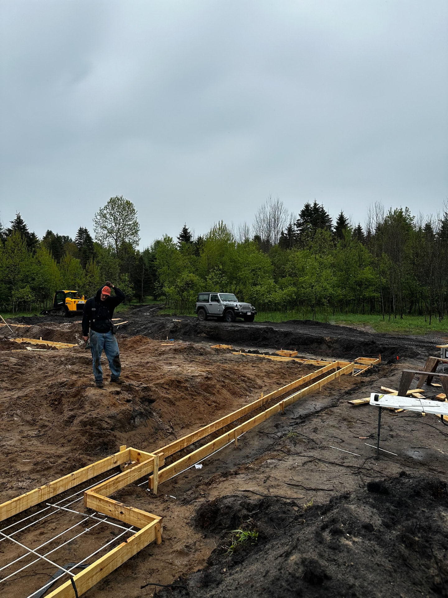 Wooden foundation forms laid out in fresh dirt where the house began, woods behind