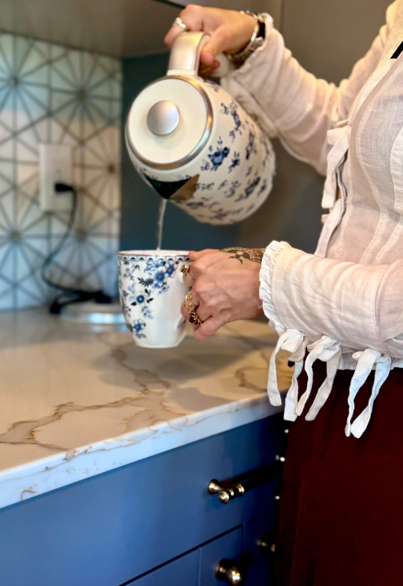 Pouring hot water from a floral kettle into a mug on the marble counter