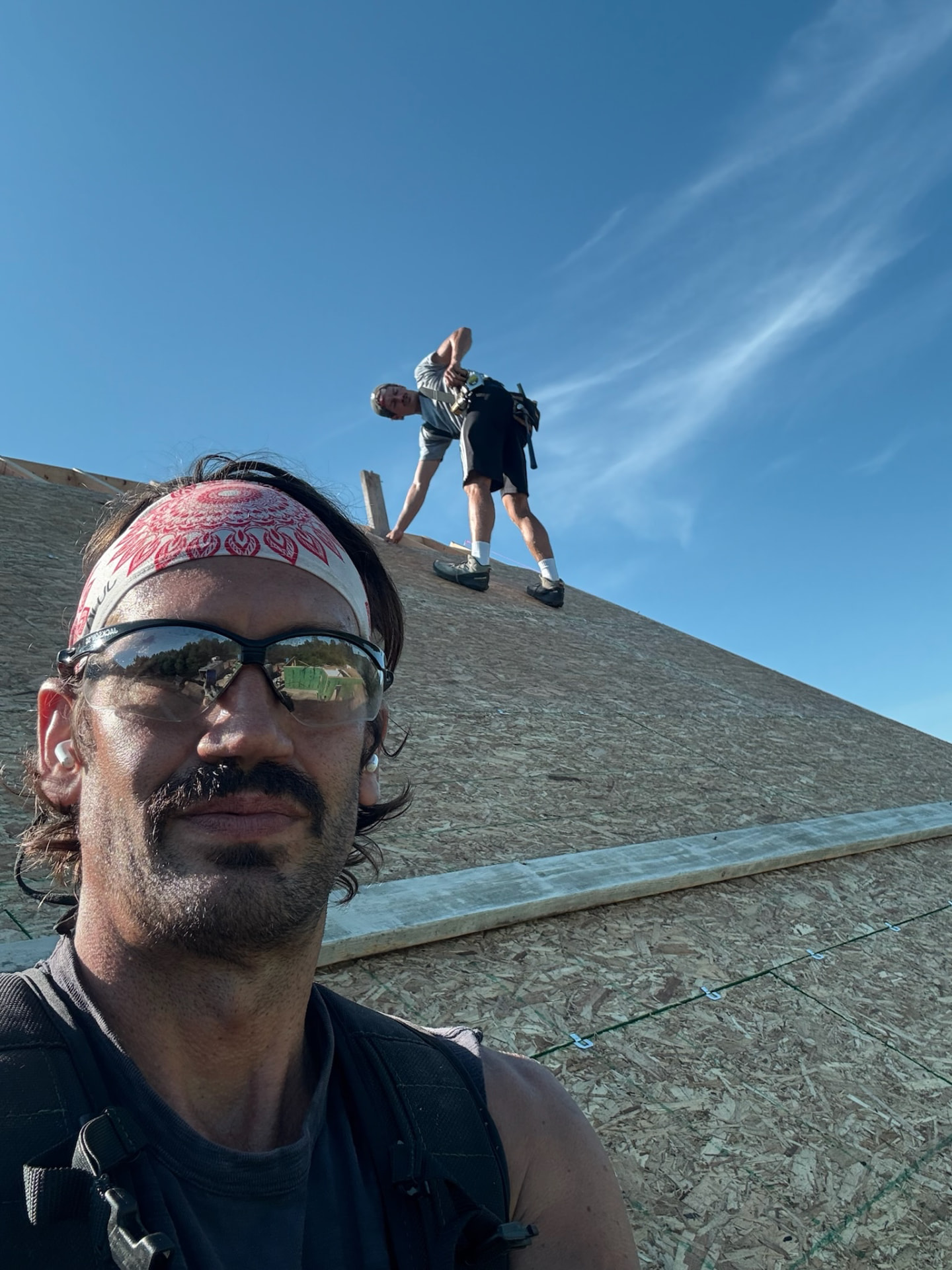 A dust-covered builder pausing for a rooftop photo while another works the ridge behind him