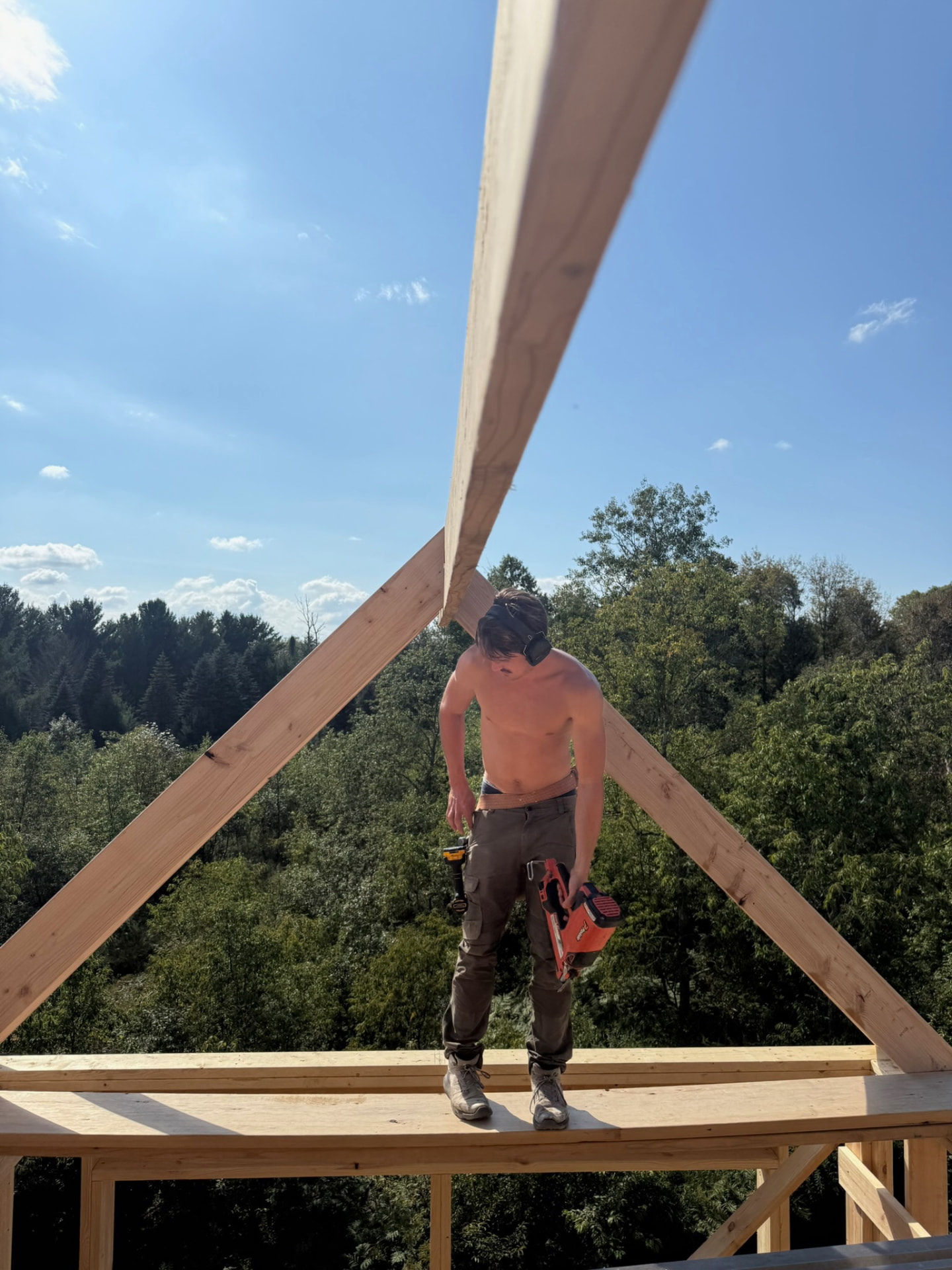 A builder raising a rafter on the framed deck, forest stretching out below