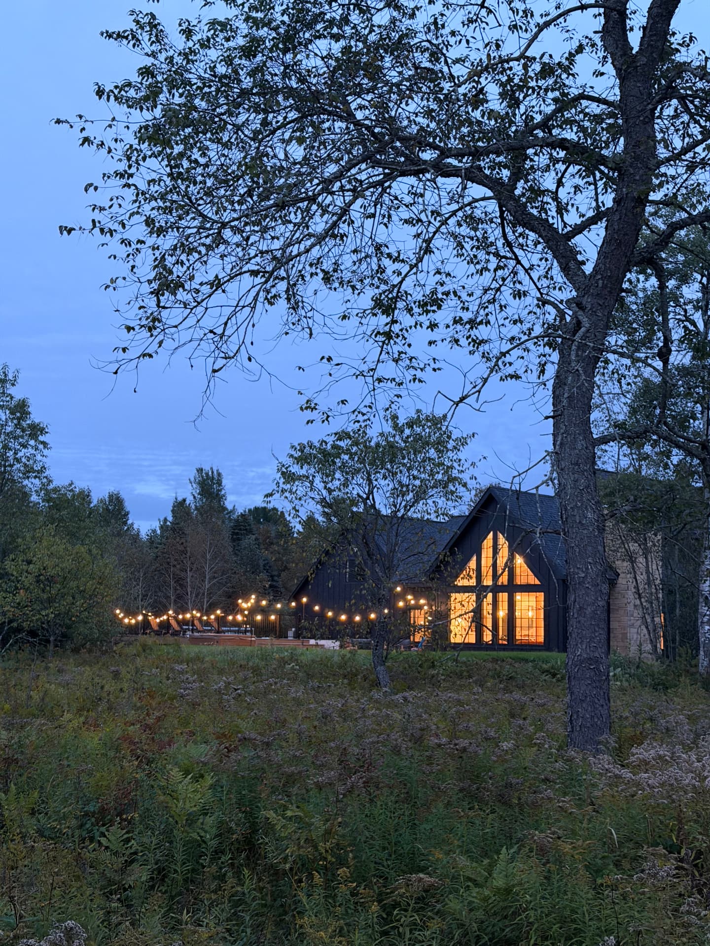 The house at dusk, windows glowing, string lights along the fence